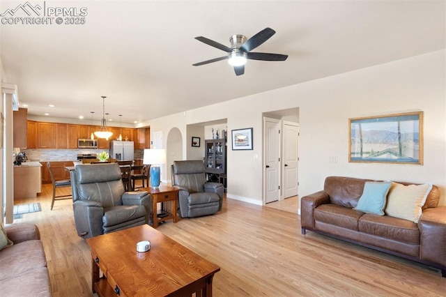 living area featuring a ceiling fan, baseboards, recessed lighting, arched walkways, and light wood-style flooring