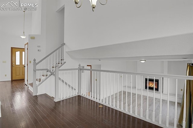 stairs featuring baseboards, wood finished floors, a towering ceiling, and a chandelier