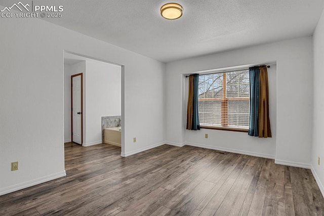 spare room featuring visible vents, baseboards, wood finished floors, and a textured ceiling