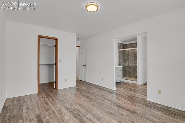unfurnished bedroom with a spacious closet, baseboards, and wood finished floors