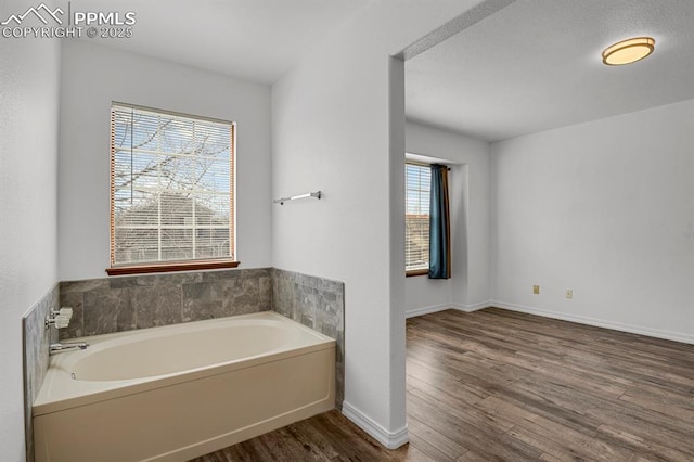 bathroom with a bath, wood finished floors, and baseboards