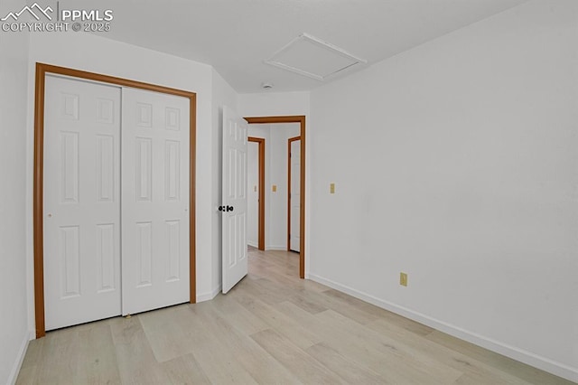 unfurnished bedroom featuring attic access, baseboards, light wood-style floors, and a closet