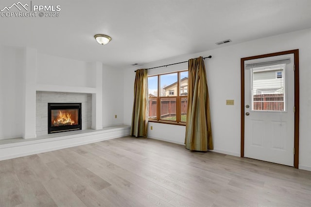 unfurnished living room with baseboards, visible vents, a fireplace, and light wood-style floors