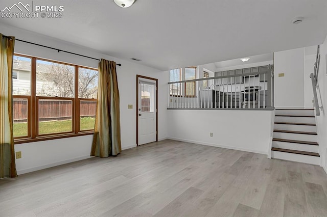 unfurnished living room with baseboards, light wood-style flooring, visible vents, and stairs
