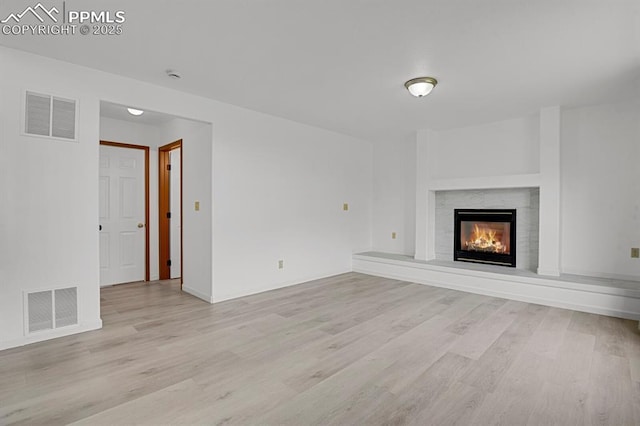 unfurnished living room with a warm lit fireplace, light wood-type flooring, and visible vents