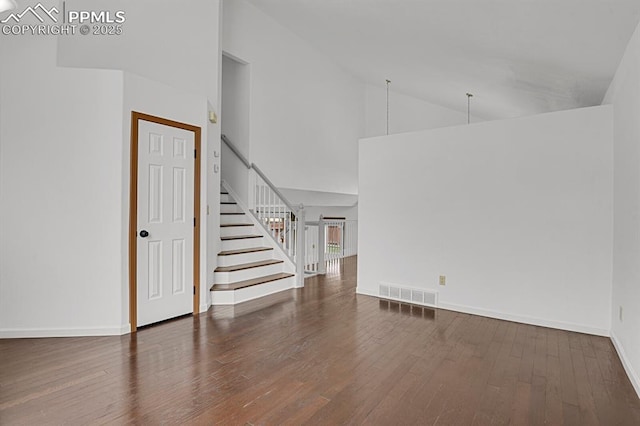 unfurnished living room with wood finished floors, visible vents, stairs, baseboards, and high vaulted ceiling