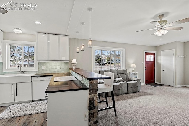 kitchen with tasteful backsplash, a sink, dishwasher, a peninsula, and white cabinetry