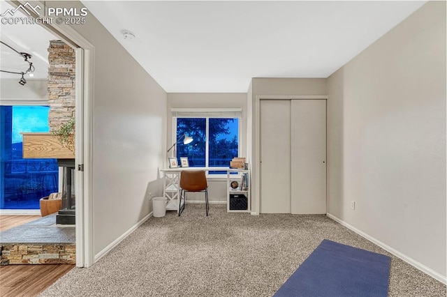carpeted office space featuring track lighting, baseboards, and a stone fireplace