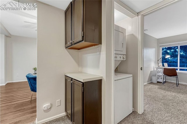 washroom featuring light colored carpet, baseboards, stacked washing maching and dryer, and laundry area