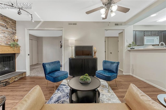 living room with ceiling fan, a fireplace, wood finished floors, and visible vents