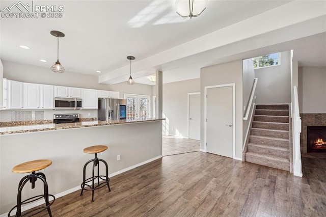 kitchen with stainless steel appliances, dark wood finished floors, a kitchen bar, white cabinetry, and decorative light fixtures
