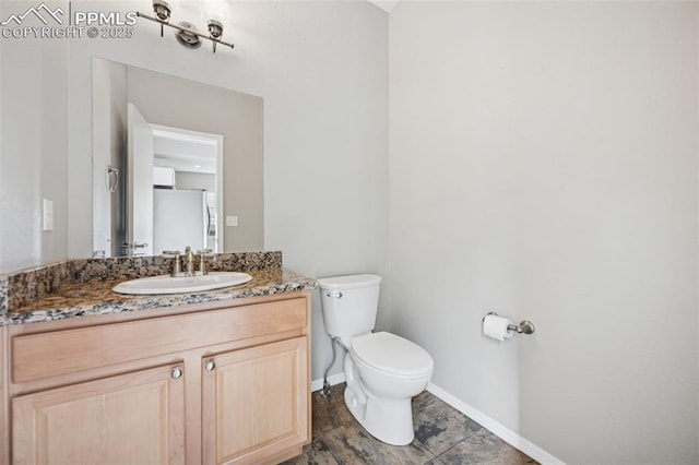 half bath with baseboards, vanity, and toilet