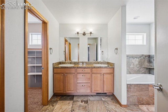 full bath with double vanity, baseboards, a relaxing tiled tub, and a sink