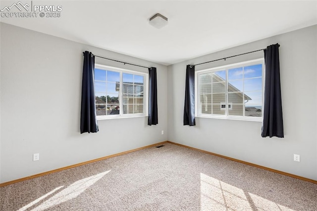 carpeted empty room featuring baseboards, a healthy amount of sunlight, and visible vents