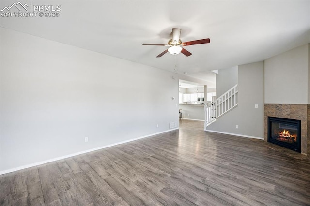unfurnished living room with a ceiling fan, wood finished floors, stairs, a tile fireplace, and baseboards