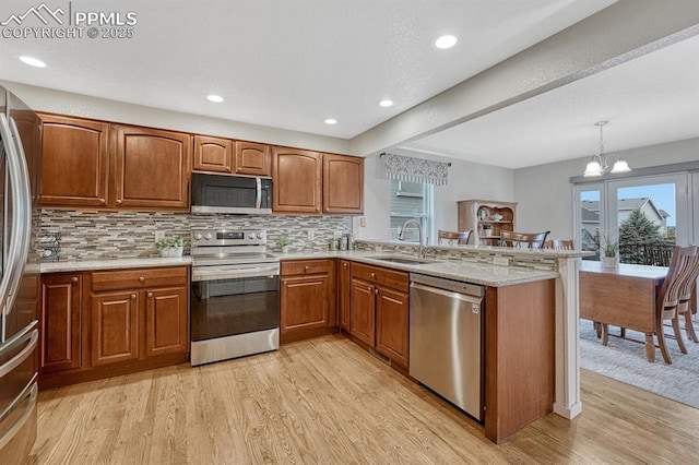 kitchen featuring stainless steel appliances, light wood-style flooring, a sink, a peninsula, and brown cabinetry
