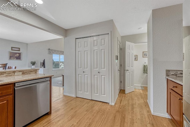 kitchen with dishwasher, brown cabinets, light wood-style floors, and light stone countertops