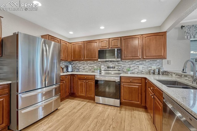 kitchen with stainless steel appliances, a sink, light wood-type flooring, light stone countertops, and brown cabinets