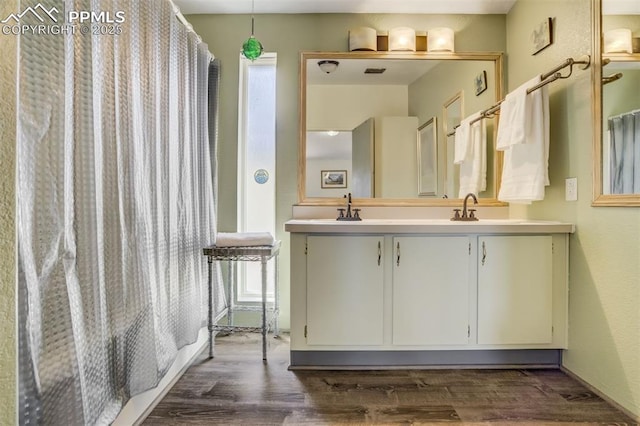 bathroom featuring double vanity, wood finished floors, a shower with shower curtain, and a sink