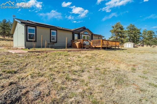 back of house with a storage shed, a deck, a yard, and an outbuilding