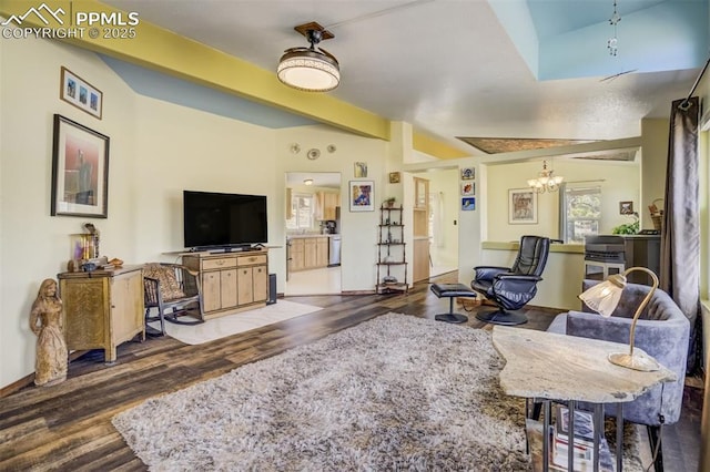 living room featuring an inviting chandelier, beam ceiling, wood finished floors, and baseboards