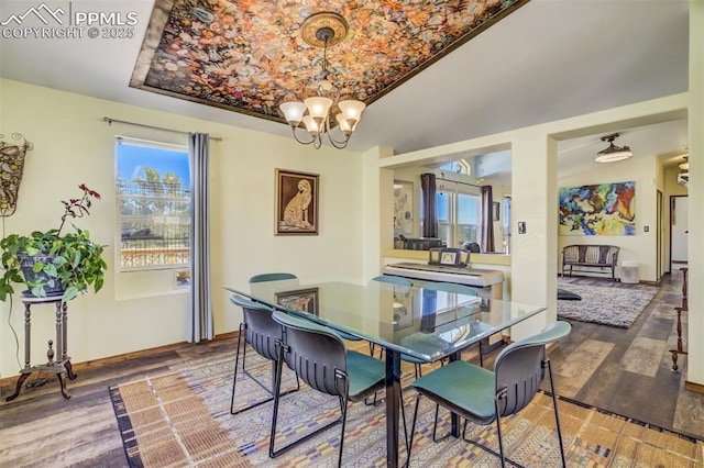 dining space with a raised ceiling, an inviting chandelier, wood finished floors, and baseboards