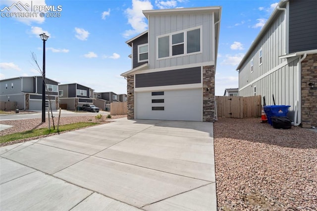 view of front of home with concrete driveway, board and batten siding, fence, a garage, and a residential view
