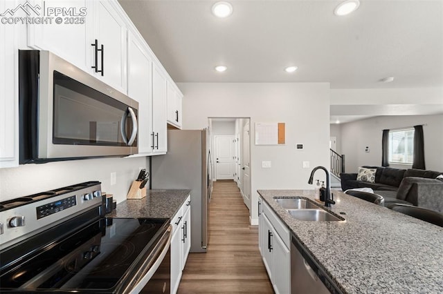 kitchen with dark wood-style floors, light stone counters, stainless steel appliances, a sink, and white cabinetry