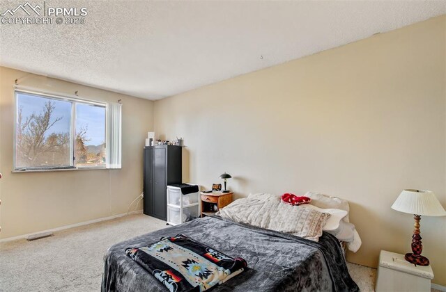 carpeted bedroom featuring a textured ceiling, visible vents, and baseboards