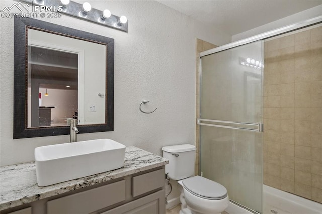 bathroom featuring a shower stall, toilet, vanity, and a textured wall