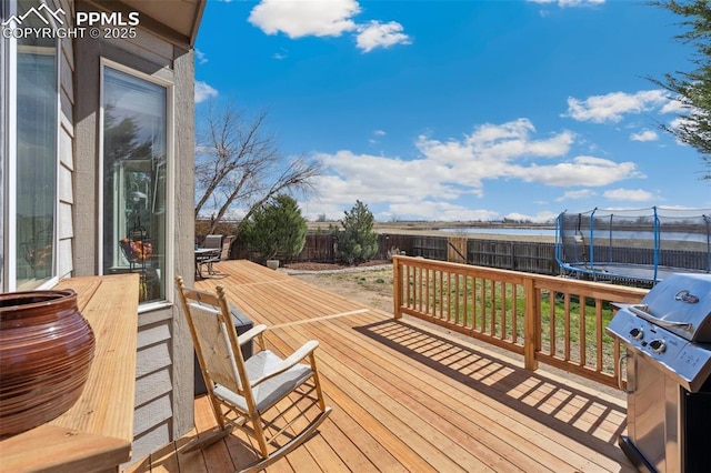 wooden terrace with a fenced backyard, a trampoline, and area for grilling