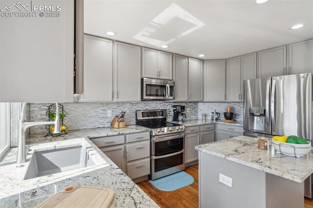 kitchen with stainless steel appliances, wood finished floors, a sink, and gray cabinets