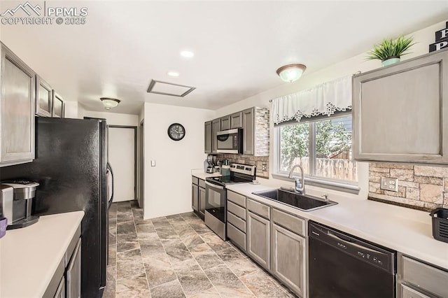 kitchen with decorative backsplash, light countertops, a sink, stone finish flooring, and black appliances