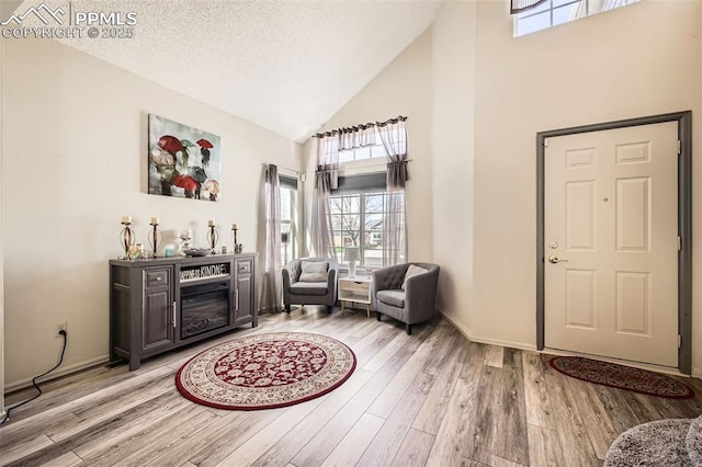 entryway featuring light wood-type flooring, a textured ceiling, baseboards, and high vaulted ceiling