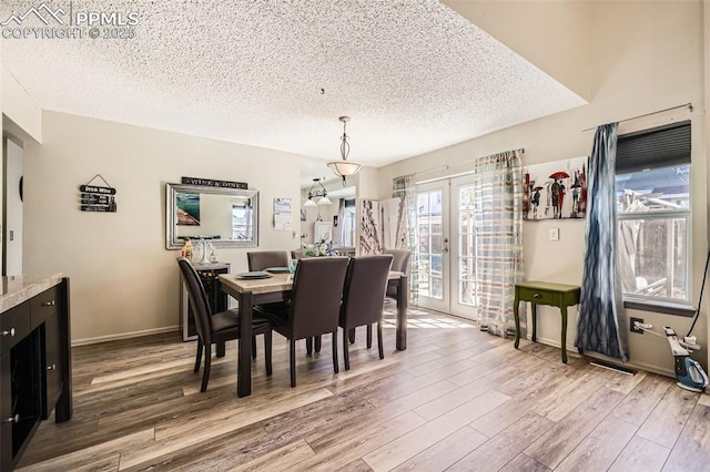 dining area featuring a healthy amount of sunlight, french doors, light wood finished floors, and a textured ceiling