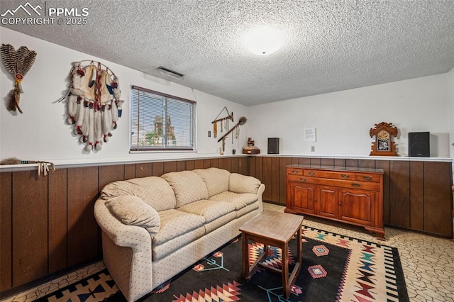 living area with visible vents, a textured ceiling, and wainscoting