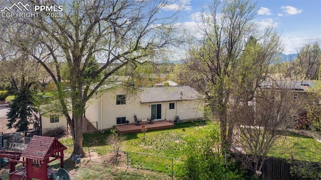 rear view of property featuring fence, a wooden deck, a lawn, and stucco siding