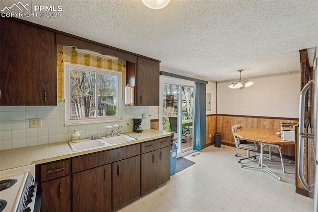 kitchen featuring a sink, wainscoting, an inviting chandelier, wood walls, and light countertops