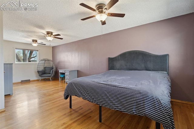 bedroom featuring ceiling fan, baseboards, wood finished floors, and a textured ceiling