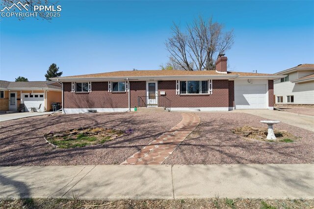 single story home featuring driveway, a chimney, brick siding, and a garage