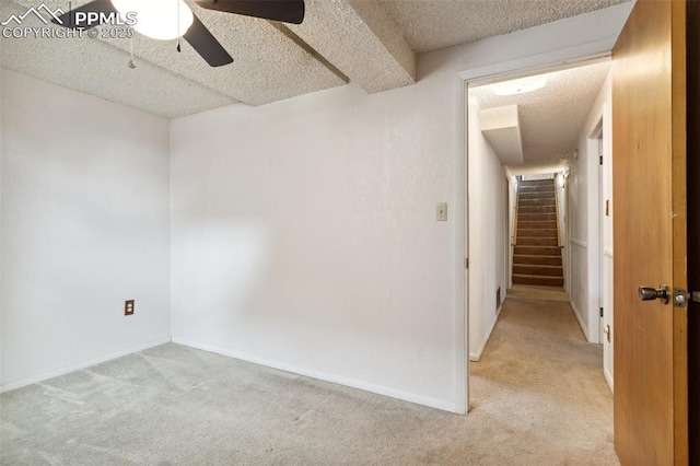 unfurnished room featuring light colored carpet, ceiling fan, a textured ceiling, and stairway