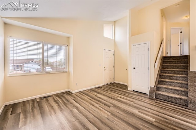 unfurnished living room with baseboards, stairway, wood finished floors, and high vaulted ceiling