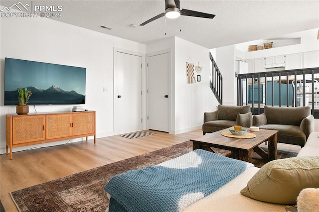 living room featuring wood finished floors, ceiling fan, stairs, and a textured ceiling