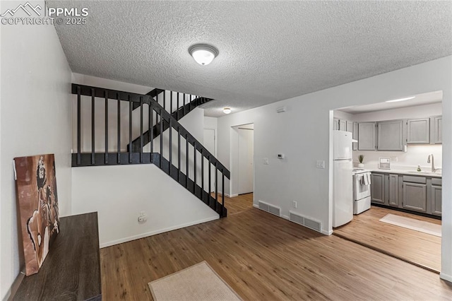 unfurnished living room with light wood-style flooring, visible vents, a sink, and a textured ceiling