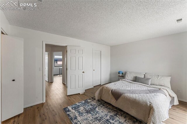 bedroom featuring wood finished floors, visible vents, and a textured ceiling
