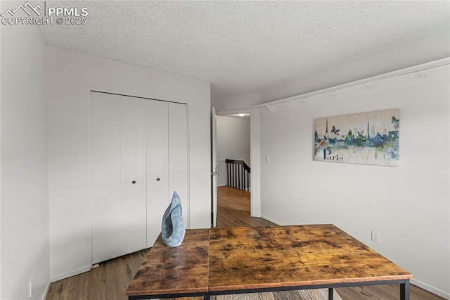 unfurnished office featuring wood finished floors, a textured ceiling, and baseboards