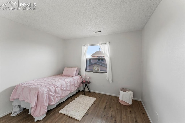 bedroom with baseboards, visible vents, wood finished floors, and a textured ceiling