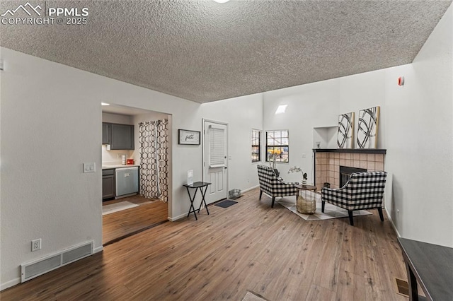 living area featuring a tiled fireplace, a textured ceiling, hardwood / wood-style floors, and visible vents