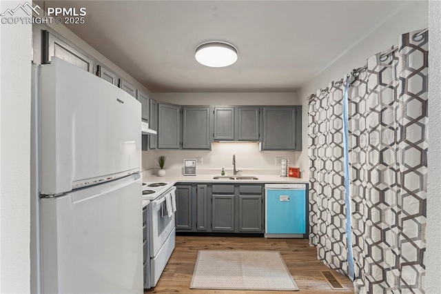 kitchen with under cabinet range hood, white appliances, a sink, and dark wood-type flooring