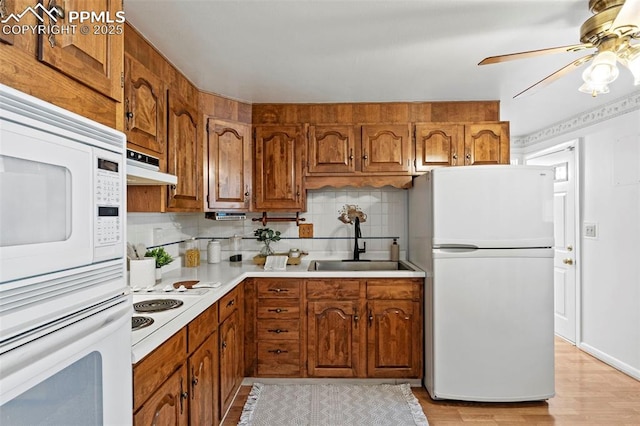kitchen featuring decorative backsplash, brown cabinets, a sink, under cabinet range hood, and white appliances